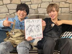 two boys sitting on a couch holding up a sign