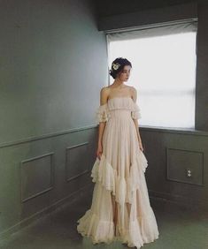 a woman standing in front of a window wearing a dress with ruffles on it