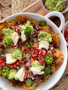 a white bowl filled with nachos on top of a wooden table next to bowls of guacamole and salsa