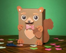 a cardboard box with a bear holding a heart on it's chest, surrounded by confetti