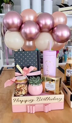 a table topped with lots of pink and gold balloons next to bottles of champagne, nuts and pineapples