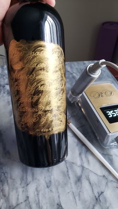 a person is holding a wine bottle with gold foil on it and an electronic device next to it