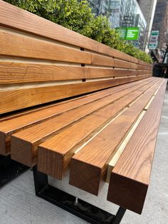 a wooden bench sitting on top of a sidewalk next to tall buildings and trees in the background