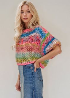 a woman wearing a multicolored sweater and denim skirt standing in front of a white wall