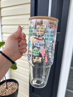 a person holding up a glass with words on it and a plant in the background