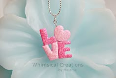 a necklace with the word love written in pink glitter on it and a flower behind it