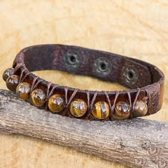 a brown leather bracelet with beads and metal fittings sits on a piece of wood