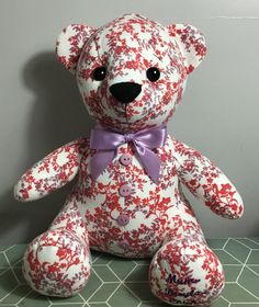 a red and white teddy bear with a purple bow tie on it's neck