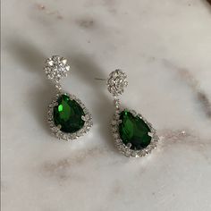 two pear shaped green and white diamond earrings on a marble countertop, with the top one being surrounded by diamonds