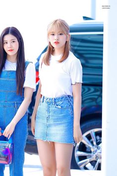 two young women standing next to each other in front of a blue car and one holding a purse