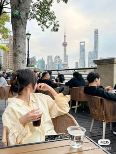 a woman sitting at a table with a drink in her hand and looking out over the city