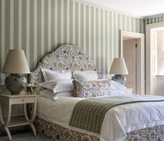 a bedroom with green and white striped wallpaper, a bed covered in pillows and blankets