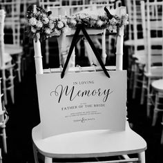 a sign that says in loving memory attached to a chair with flowers on it at a wedding