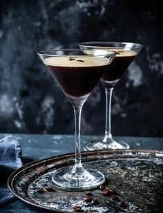 two glasses filled with liquid sitting on top of a metal tray next to each other