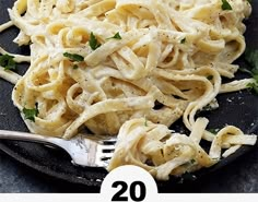 a black plate topped with pasta covered in sauce and parsley next to a fork