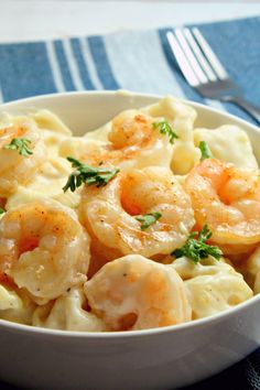 a bowl filled with pasta and shrimp on top of a blue table cloth next to a fork