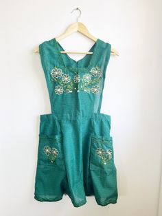 a green dress hanging on a white wall next to a wooden hanger with an object in it