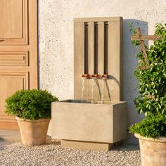 an outdoor fountain surrounded by two potted plants and a wooden door in the background