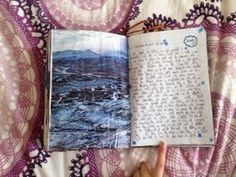 an open book sitting on top of a bed next to a person's hand