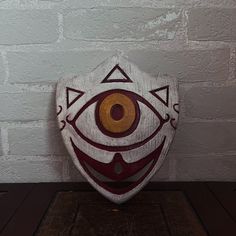 a mask with an eye painted on it sitting in front of a brick wall next to a wooden table