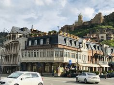 cars are driving down the street in front of buildings on a hill with castle like structures