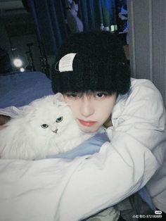 a person holding a white cat wearing a black beanie hat on top of their head