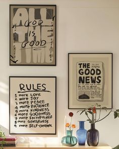 three framed posters hang on the wall above a wooden table with vases and flowers