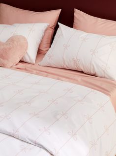 a bed with pink and white sheets, pillows and a heart shaped pillow on it