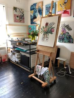 an artist's easel in front of several paintings on the wall and floor