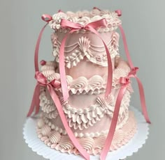 a three tiered cake with pink icing and ribbon on top, sitting on a white plate