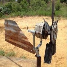 an airplane propeller on top of a wooden pole in the dirt near trees and bushes