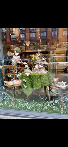 a window display with chairs and tables covered in flowers, grass and other things inside