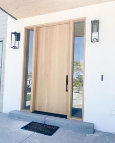 the front door to a house with a welcome mat and light fixture on either side