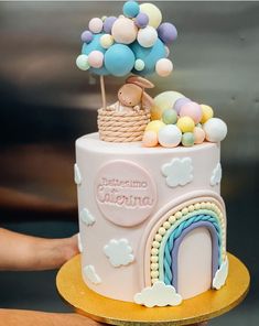 there is a pink cake with balloons on the top and rainbows in the middle