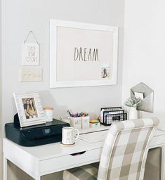 a white desk topped with a laptop computer next to a printer and pictures on the wall