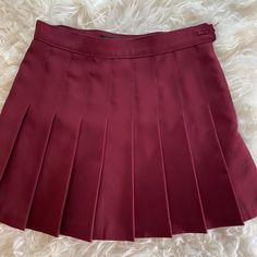 a maroon pleated skirt is laying on a white furnishing area, with the bottom section showing