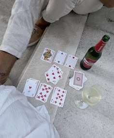 the man is sitting on the floor playing cards and drinking some wine next to him