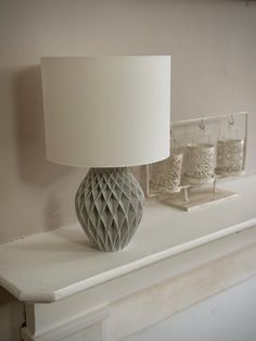 a lamp sitting on top of a white mantle next to two glass jars and a mirror