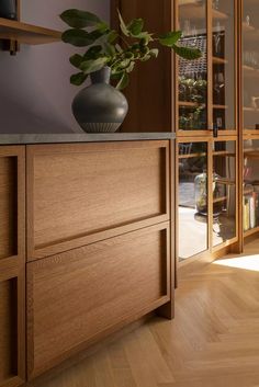 a vase with a plant in it on top of a wooden cabinet next to a window