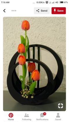 three orange tulips in a black vase with greenery on the bottom and two green stems sticking out of it