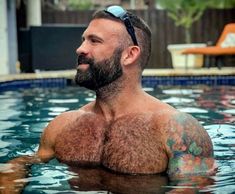 a man with tattoos on his chest in a pool looking off into the distance while wearing goggles