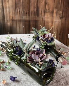 two wine bottles filled with succulents and greenery on a white table cloth