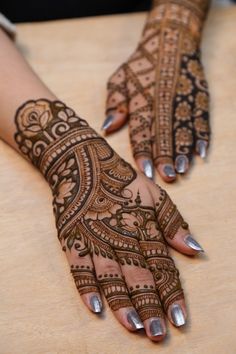 two hands with henna tattoos on them sitting on a wooden table next to each other