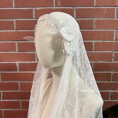 a mannequin wearing a white veil with flowers on the head and neck, in front of a brick wall