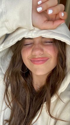 a woman with her eyes closed wearing a white hoodie and smiling at the camera