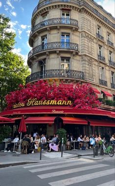 people sitting at tables in front of a building with red awnings and flowers on it