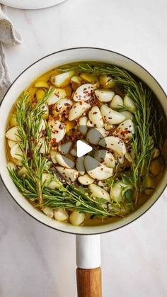 a pot filled with potatoes and herbs on top of a white counter next to a wooden spoon