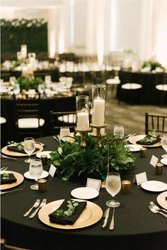 the table is set with place settings for dinner and wine glasses, candles, and greenery