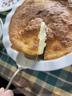 a person is holding a spoon over a cake on a plate with a slice missing