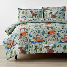 a bed covered in a comforter with animals and trees on it's cover